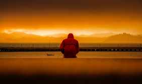 person wearing red hoodie sitting in front of body of water
